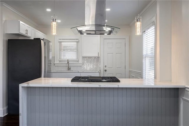 kitchen with light stone countertops, island exhaust hood, freestanding refrigerator, white cabinets, and crown molding