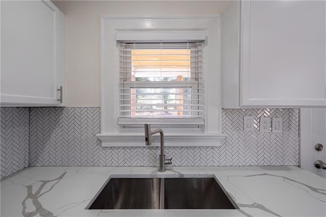 kitchen featuring a sink, decorative backsplash, light stone countertops, and white cabinets