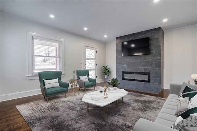 living area with a tiled fireplace, ornamental molding, and wood finished floors