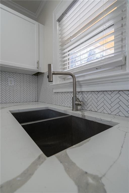 details featuring light stone countertops, a sink, white cabinetry, crown molding, and tasteful backsplash