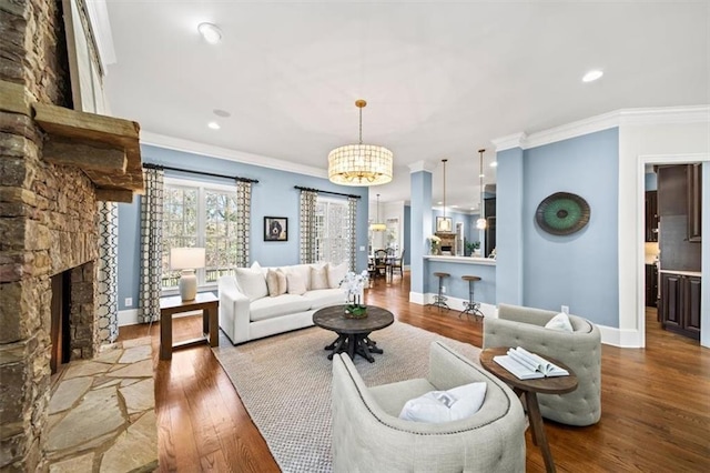 living room featuring wood-type flooring, ornamental molding, a notable chandelier, and a fireplace