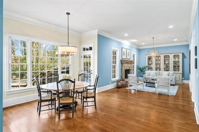 dining space with an inviting chandelier, a stone fireplace, ornamental molding, and hardwood / wood-style floors