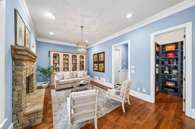 living room featuring a stone fireplace, ornamental molding, dark wood-type flooring, and an inviting chandelier