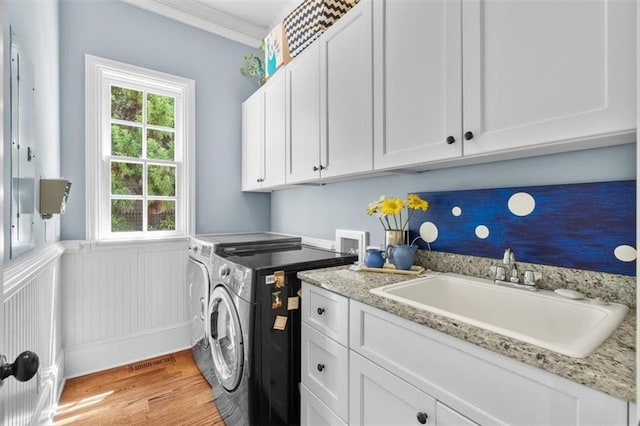 washroom with crown molding, washing machine and clothes dryer, sink, light wood-type flooring, and cabinets