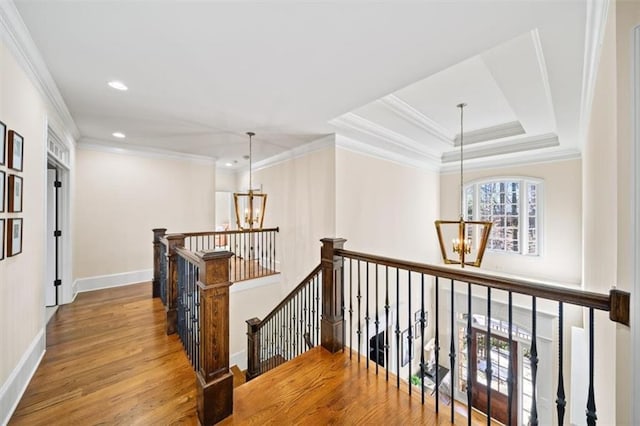 corridor featuring light wood-type flooring, a tray ceiling, a notable chandelier, and ornamental molding