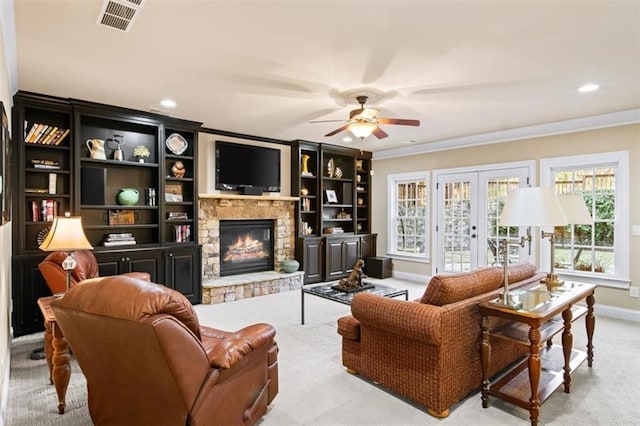 carpeted living room with french doors, a stone fireplace, ceiling fan, and ornamental molding