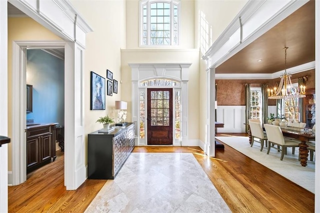 foyer featuring light hardwood / wood-style floors, a towering ceiling, a notable chandelier, and ornamental molding