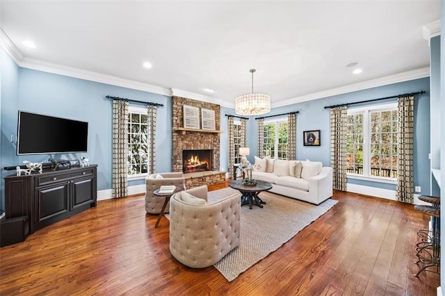 living room with a stone fireplace, hardwood / wood-style floors, crown molding, and a notable chandelier