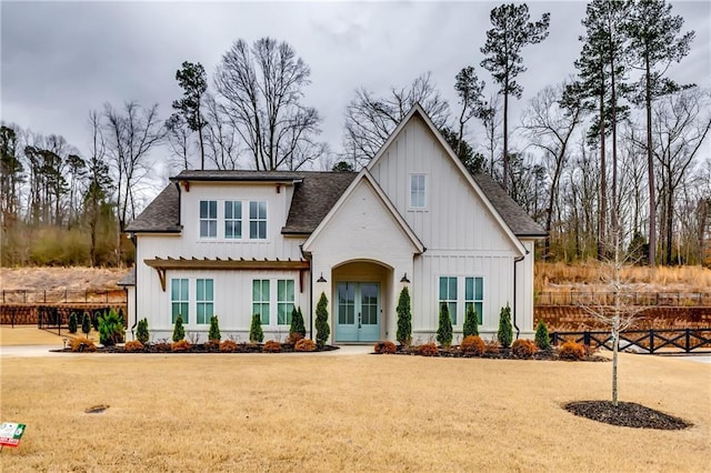 view of front of house with board and batten siding, a front yard, french doors, and fence