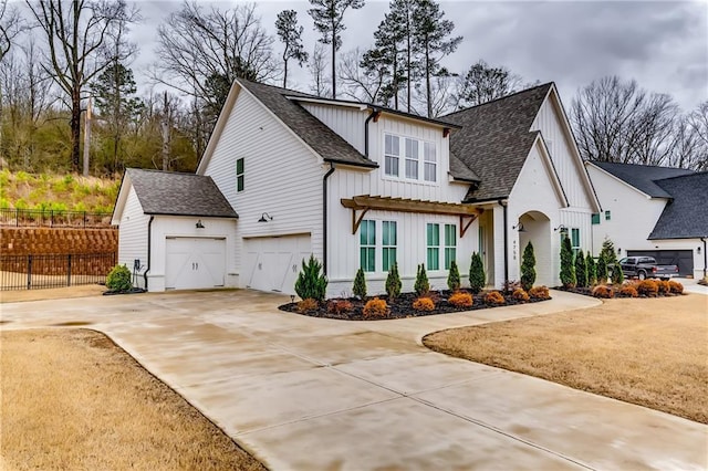 modern farmhouse style home featuring driveway, a shingled roof, an attached garage, fence, and board and batten siding