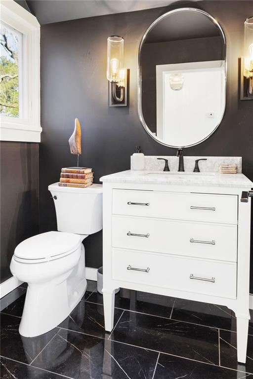 half bathroom with marble finish floor, toilet, and vanity