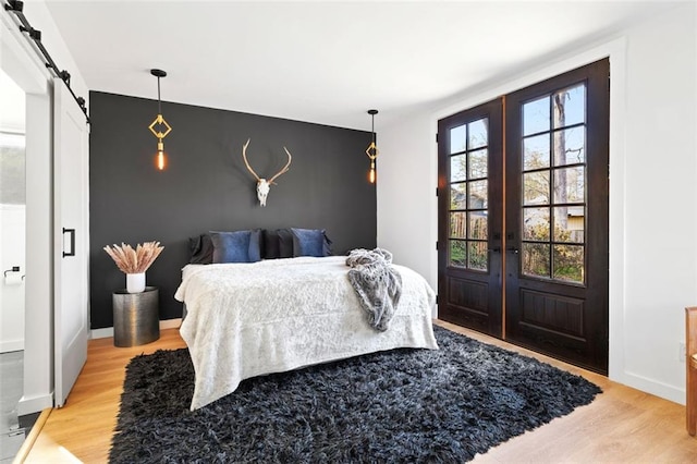 bedroom featuring a barn door, multiple windows, french doors, and light wood finished floors