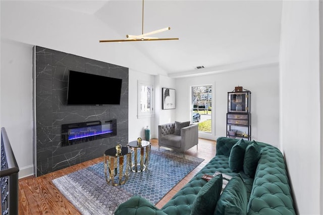 living room with visible vents, baseboards, lofted ceiling, a premium fireplace, and wood finished floors