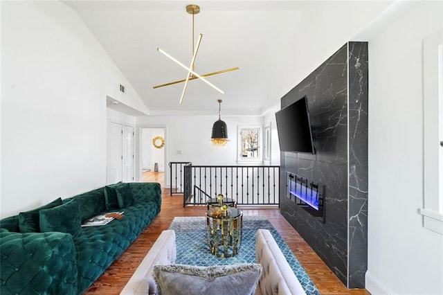 living room with a high end fireplace, visible vents, baseboards, vaulted ceiling, and wood finished floors