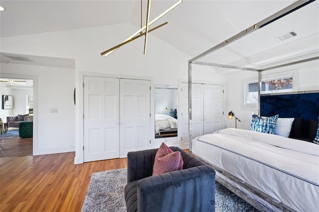 bedroom with visible vents, multiple closets, lofted ceiling, and wood finished floors