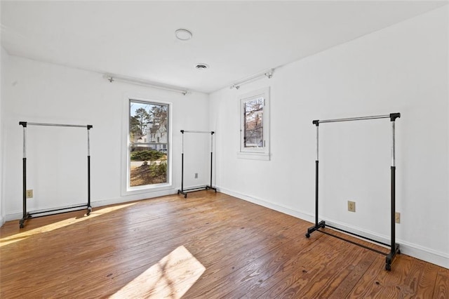 unfurnished room featuring visible vents, a healthy amount of sunlight, baseboards, and wood finished floors