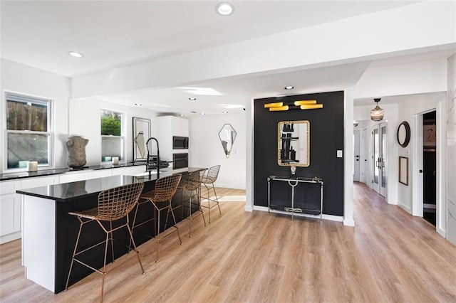 kitchen with a kitchen bar, black appliances, dark countertops, white cabinets, and light wood finished floors