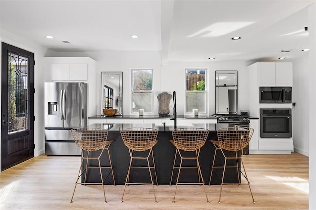 kitchen with dark countertops, a kitchen bar, appliances with stainless steel finishes, light wood-style floors, and white cabinets