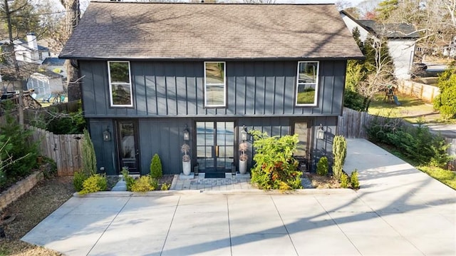 rear view of property featuring board and batten siding, roof with shingles, and fence