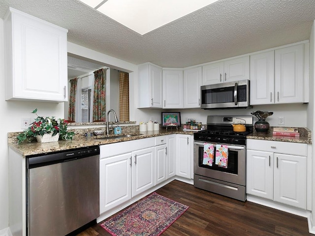 kitchen featuring sink, white cabinetry, appliances with stainless steel finishes, dark hardwood / wood-style floors, and dark stone counters