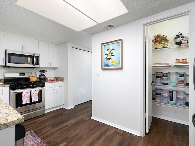 kitchen with appliances with stainless steel finishes, dark hardwood / wood-style floors, light stone counters, a textured ceiling, and white cabinets