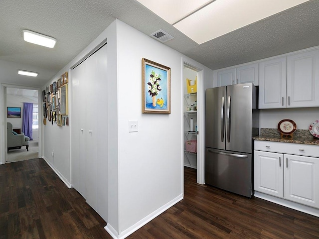 kitchen with stainless steel refrigerator, dark wood-type flooring, a textured ceiling, and white cabinets