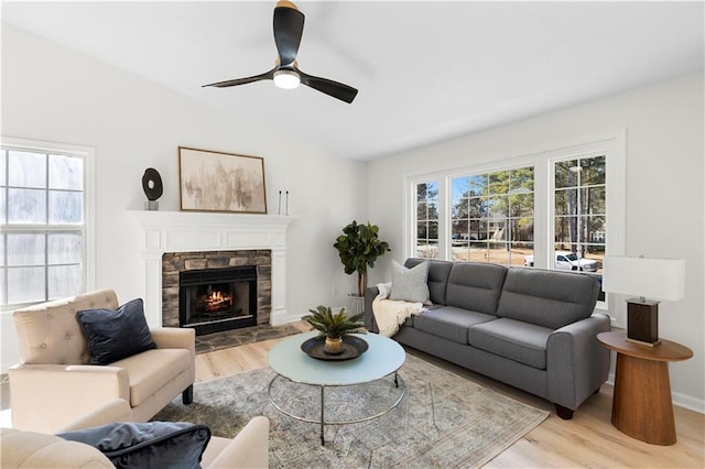 living room with light wood-type flooring, ceiling fan, and a stone fireplace