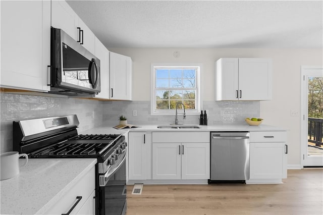 kitchen with stainless steel appliances, white cabinetry, light hardwood / wood-style floors, and sink