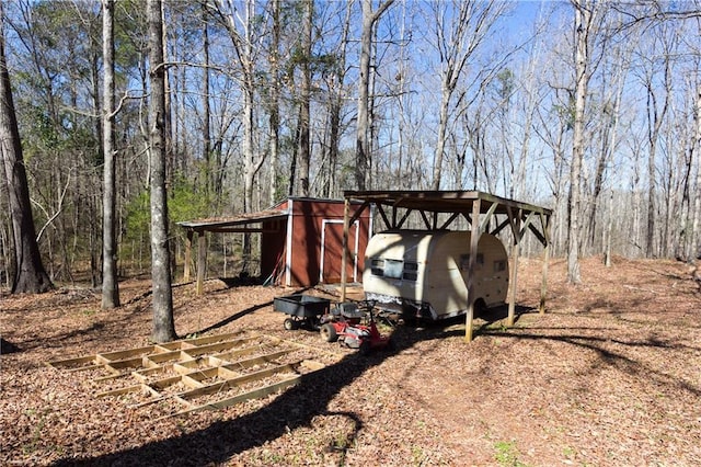 view of yard featuring a forest view, dirt driveway, and a carport