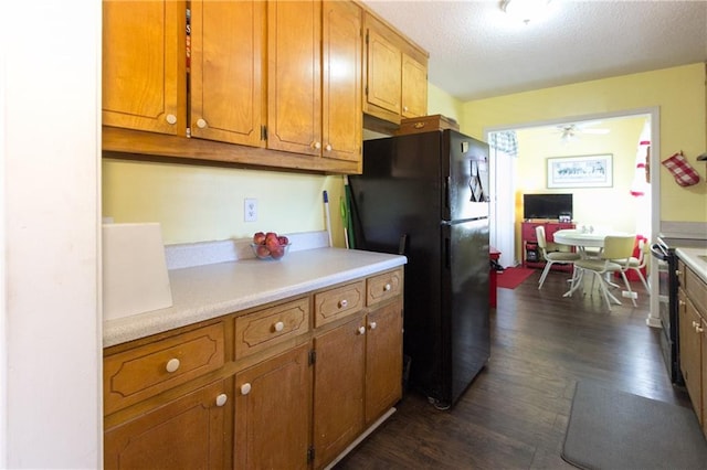 kitchen featuring brown cabinetry, dark wood-style floors, light countertops, a textured ceiling, and black appliances