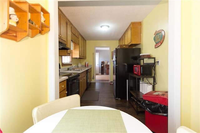 kitchen featuring brown cabinets, under cabinet range hood, light countertops, black appliances, and a sink