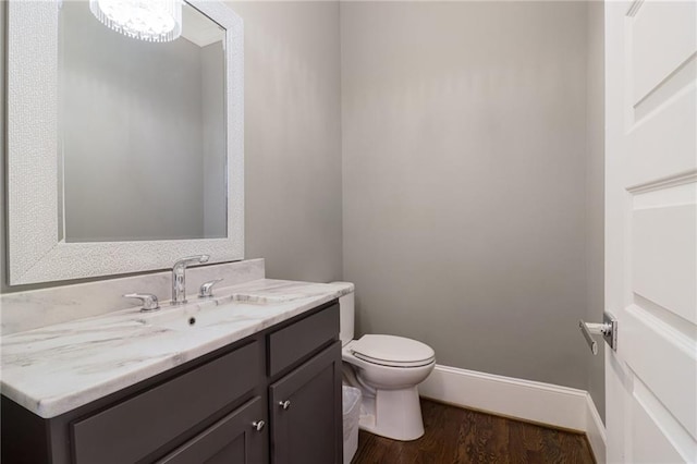 half bath featuring vanity, toilet, wood finished floors, and baseboards