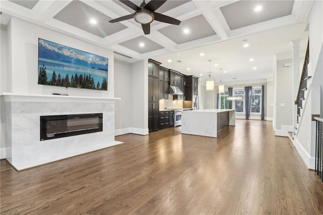 unfurnished living room with ceiling fan, dark wood-style flooring, a fireplace, coffered ceiling, and a sink