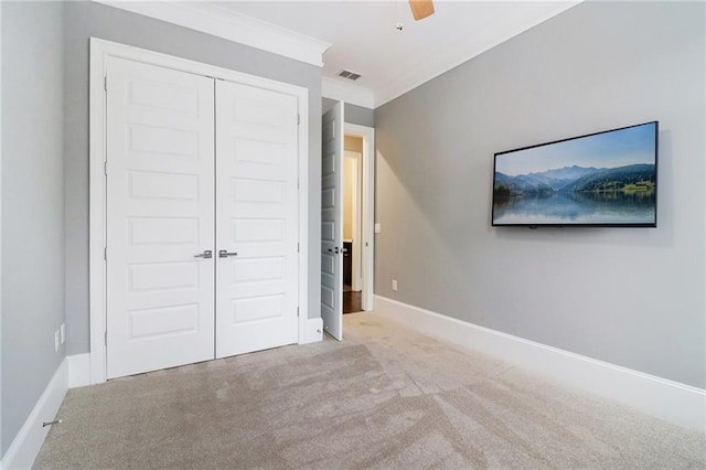 unfurnished bedroom with a ceiling fan, baseboards, a closet, crown molding, and carpet flooring