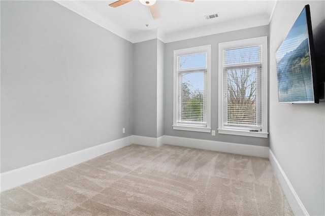 carpeted empty room featuring visible vents, baseboards, ornamental molding, and a ceiling fan