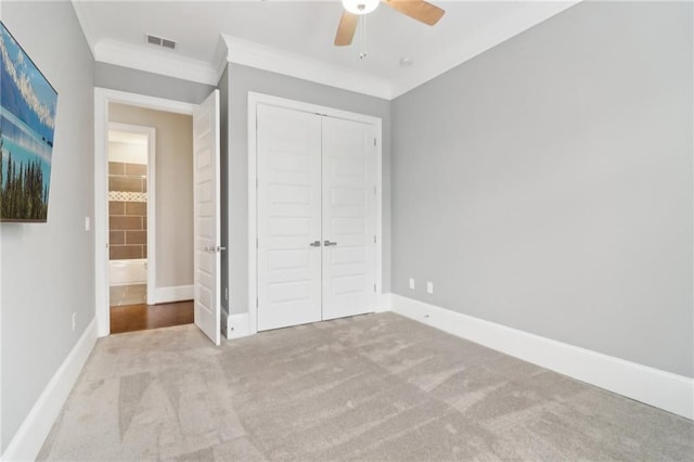 unfurnished bedroom featuring visible vents, a closet, carpet floors, crown molding, and baseboards