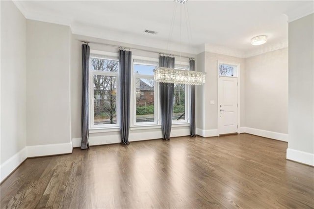 spare room featuring wood finished floors, visible vents, baseboards, an inviting chandelier, and crown molding