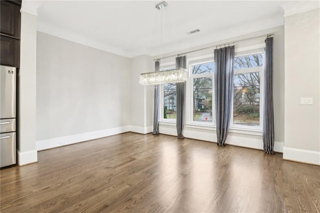 empty room featuring wood finished floors, visible vents, baseboards, an inviting chandelier, and crown molding