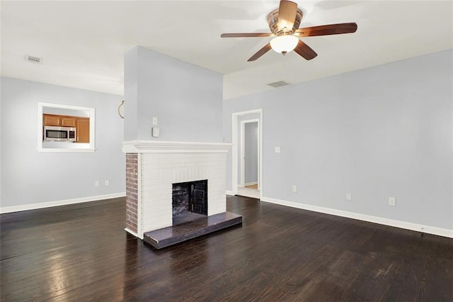 unfurnished living room featuring ceiling fan, a brick fireplace, and dark hardwood / wood-style floors