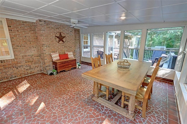 unfurnished dining area featuring brick wall, dark tile flooring, a drop ceiling, and ceiling fan