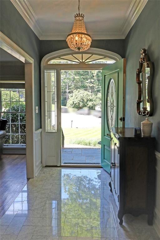 entryway with a chandelier, ornamental molding, light tile floors, and a wealth of natural light