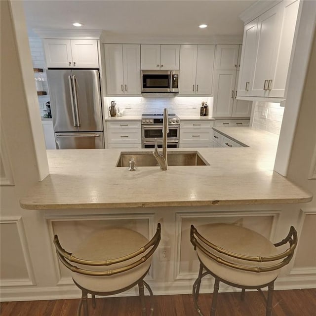 kitchen featuring tasteful backsplash, high end appliances, a kitchen breakfast bar, kitchen peninsula, and white cabinets