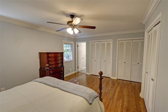 bedroom with dark hardwood / wood-style flooring, ceiling fan, two closets, and crown molding