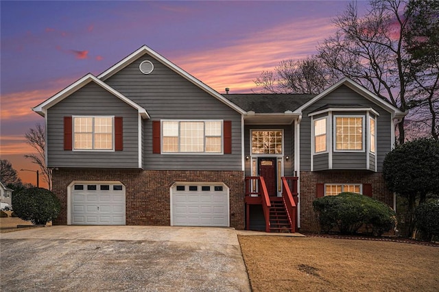 raised ranch featuring a garage, concrete driveway, and brick siding