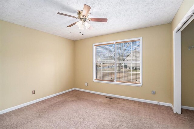 carpeted empty room featuring a ceiling fan, visible vents, a textured ceiling, and baseboards