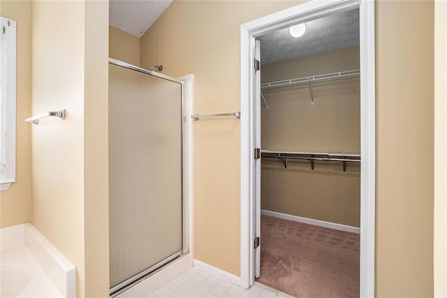 full bathroom featuring a stall shower, a textured ceiling, baseboards, and a spacious closet