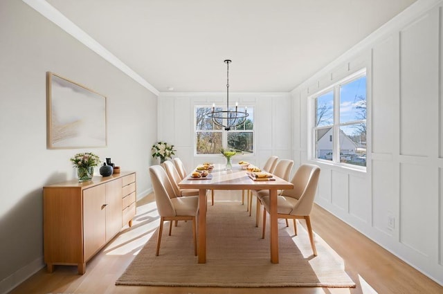 dining space with a chandelier, a decorative wall, light wood-style floors, and ornamental molding