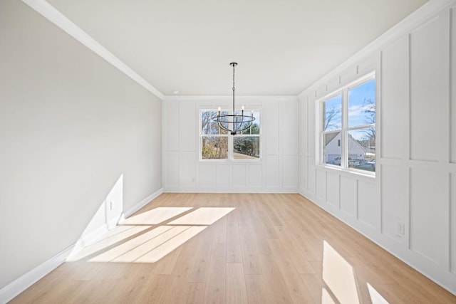 unfurnished dining area featuring a decorative wall, a notable chandelier, light wood finished floors, and ornamental molding