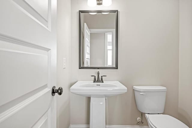 half bath with toilet, baseboards, and a sink