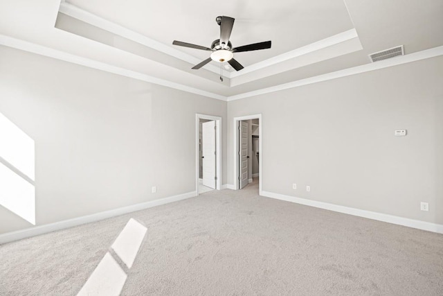 spare room with a tray ceiling, baseboards, visible vents, and ornamental molding